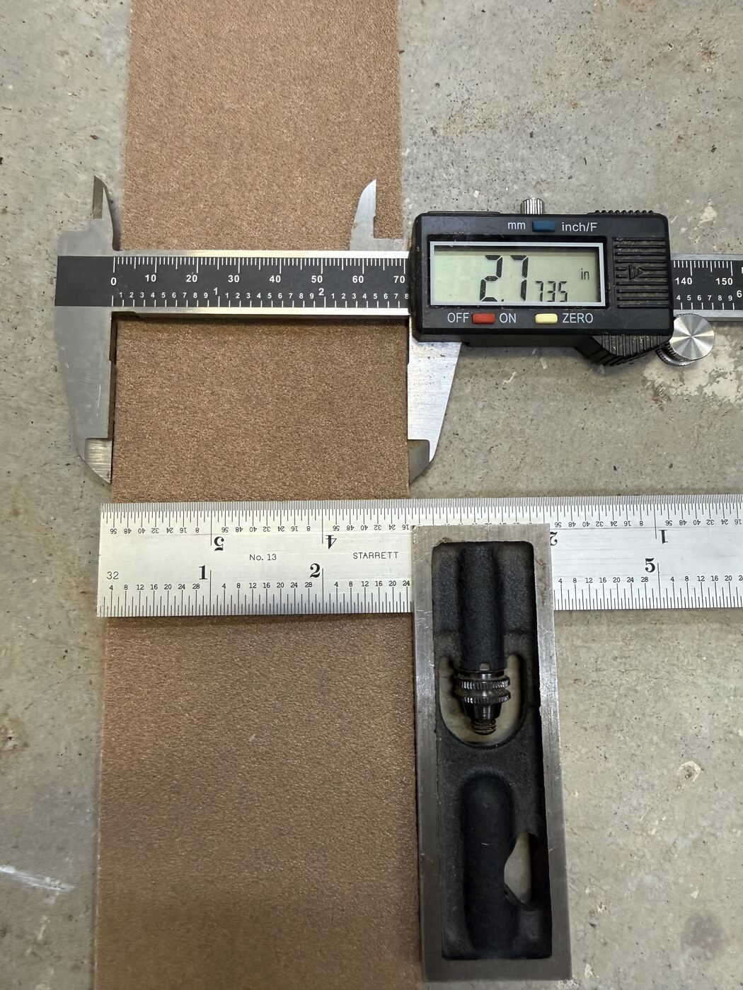 Digital calipers measuring the width of a roll of sandpaper stock.