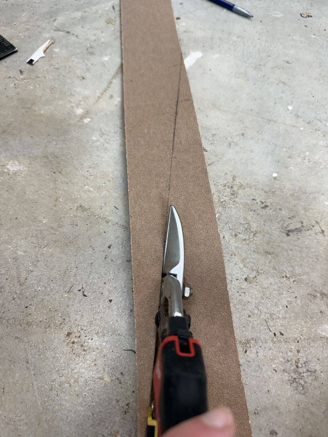 Aviation snips cutting along a marked diagonal line on the sandpaper strip.